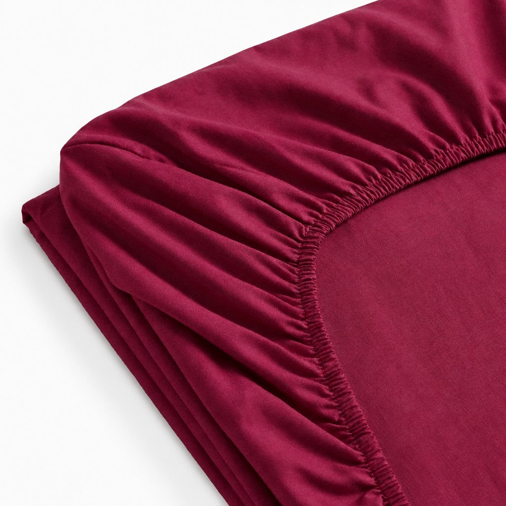 Drap-housse uni en percale de coton 100 fils/cm², finition lisse et respirante, maintien optimal avec bonnets ajustés et élastique, confection européenne durable.
